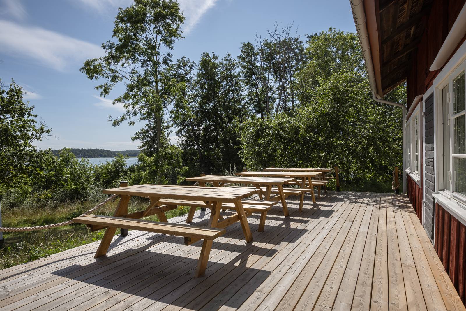 Strandkökets altan längs stugan med picknickbord och sjöutsikt